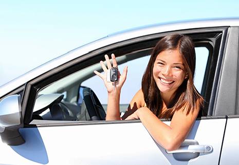 A woman holding up her car keys in the drivers seat.