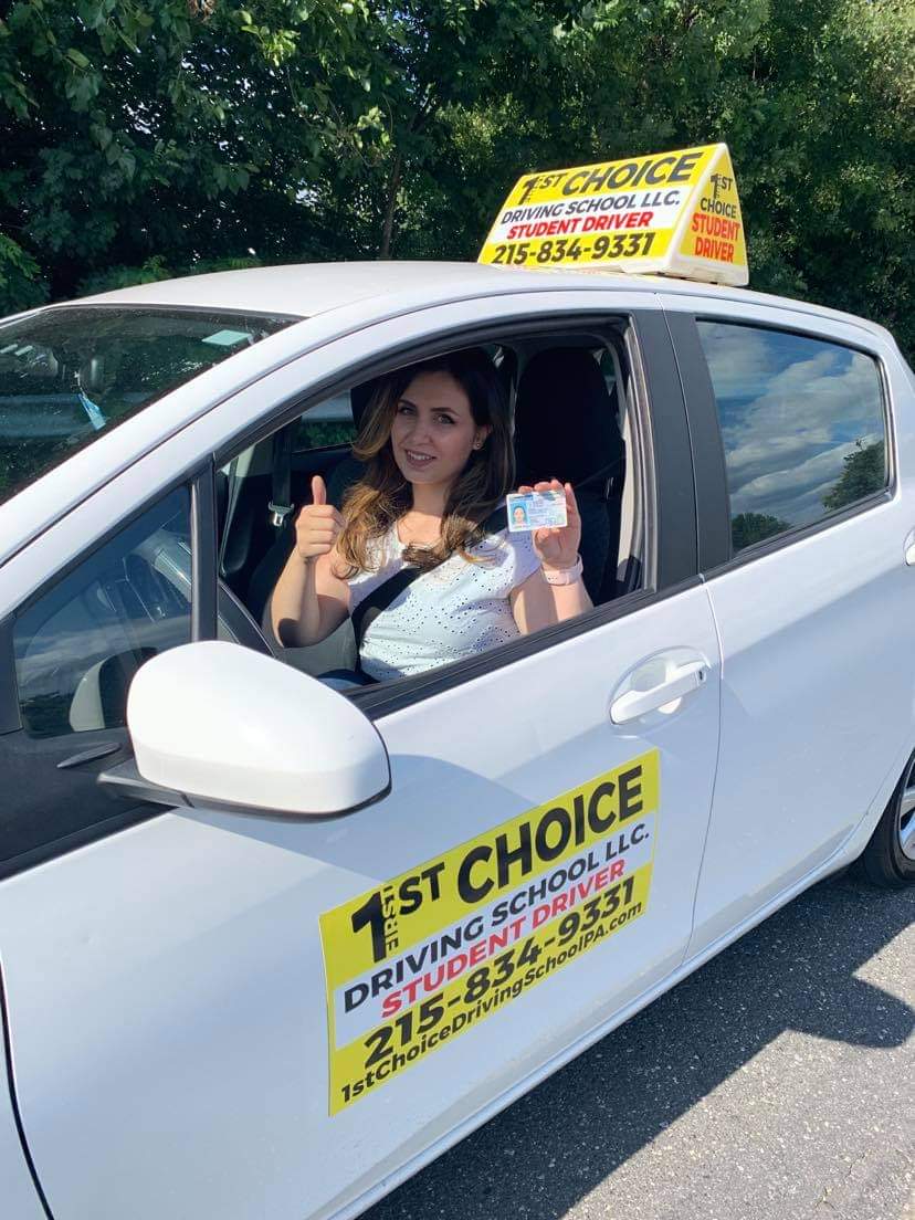 A woman in the driver 's seat of her car holding up two thumbs.